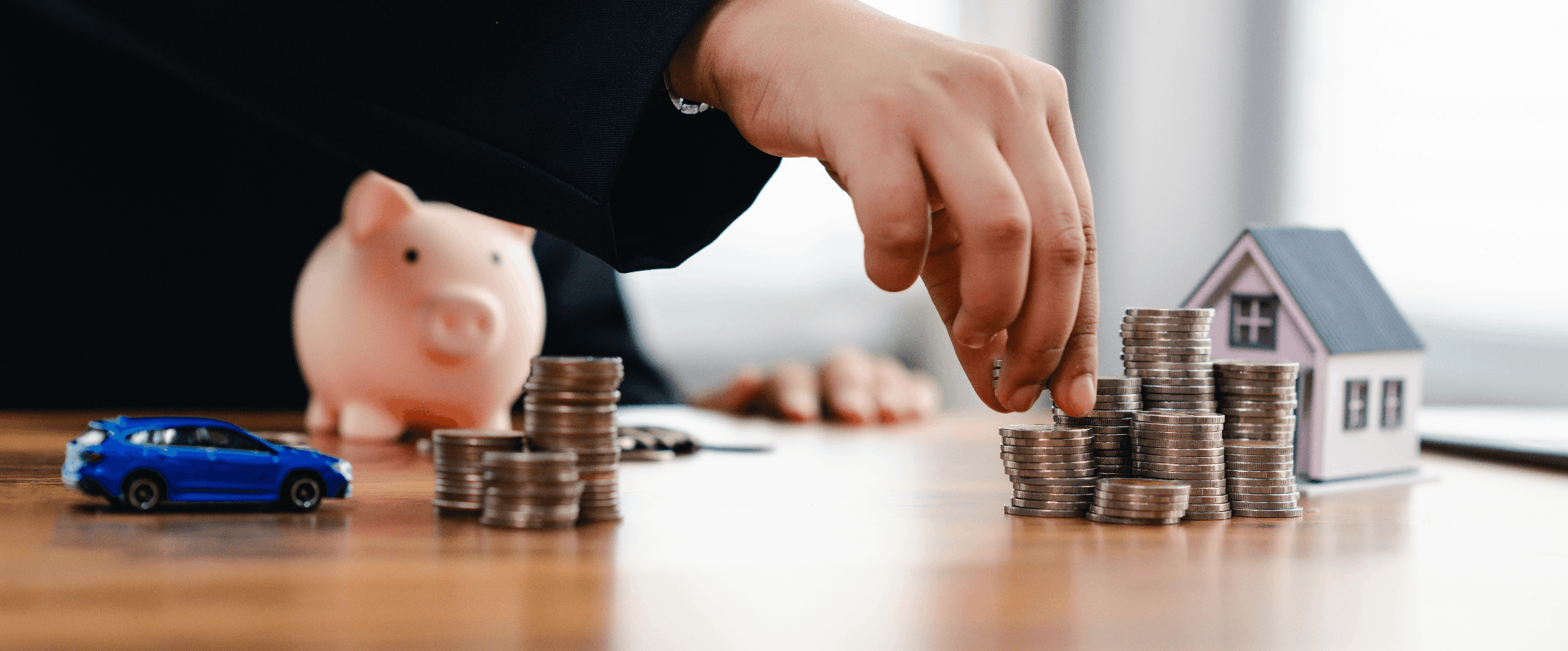 Image of a man's hand arranging coins with a car and house mockup nearby